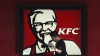 Un hombre andando cerca del logotipo de KFC, fuera de un restaurante.
