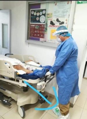 Personal del OPD Servicios de Salud del Municipio de Zapopan (SSMZ), fotografía en que se oberva a un trabajador usando simples bolsas de plástico en sus pies para proteger su calzado mientras atiende a un paciente sospechoso de covid-19.