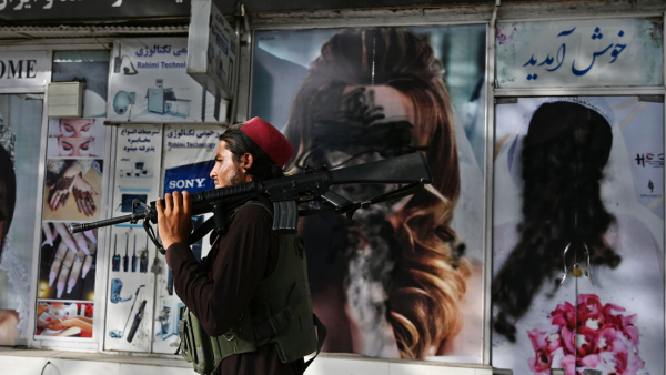 Un talibán pasa frente salón de belleza con imágenes de mujeres emborronadas en Kabul, Afganistán, el 18 de agosto de 2021. 