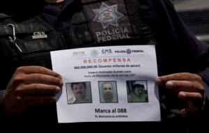 Un policía muestra el letrero de "Se Busca" de El Chapo.