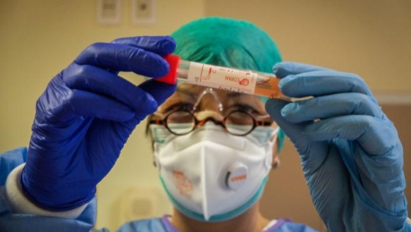 Un profesional sanitario con un traje protector y una máscara de atención médica inspecciona un vial que contiene una muestra en un laboratorio de pruebas de coronavirus Covid-19 en Cremona, Italia.