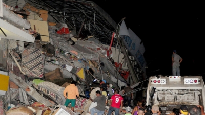 Varias personas junto a un edificio derribado por el terremoto en la ciudad costera de Manta, Ecuador.